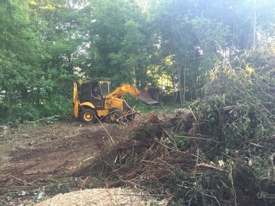 Backhoe pushing away large debris and brush for clean out