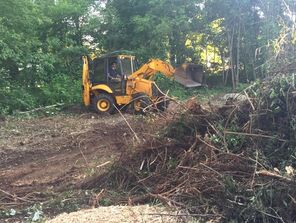 Backhoe cleaning up brush and debris in yard